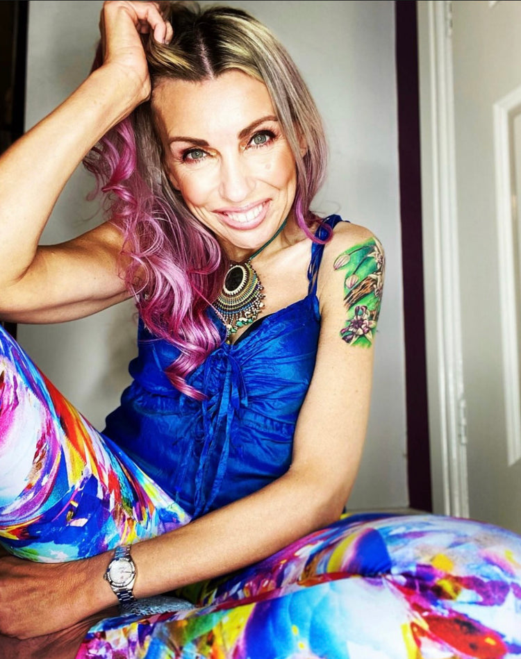 Smiling woman with pink hair in a blue top and colorful abstract-print leggings