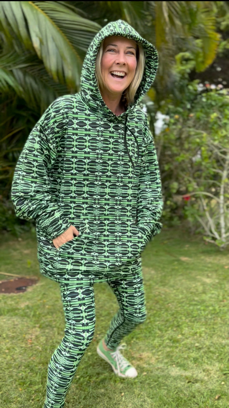 Laughing woman in a matching green print hoodie and leggings on a garden lawn
