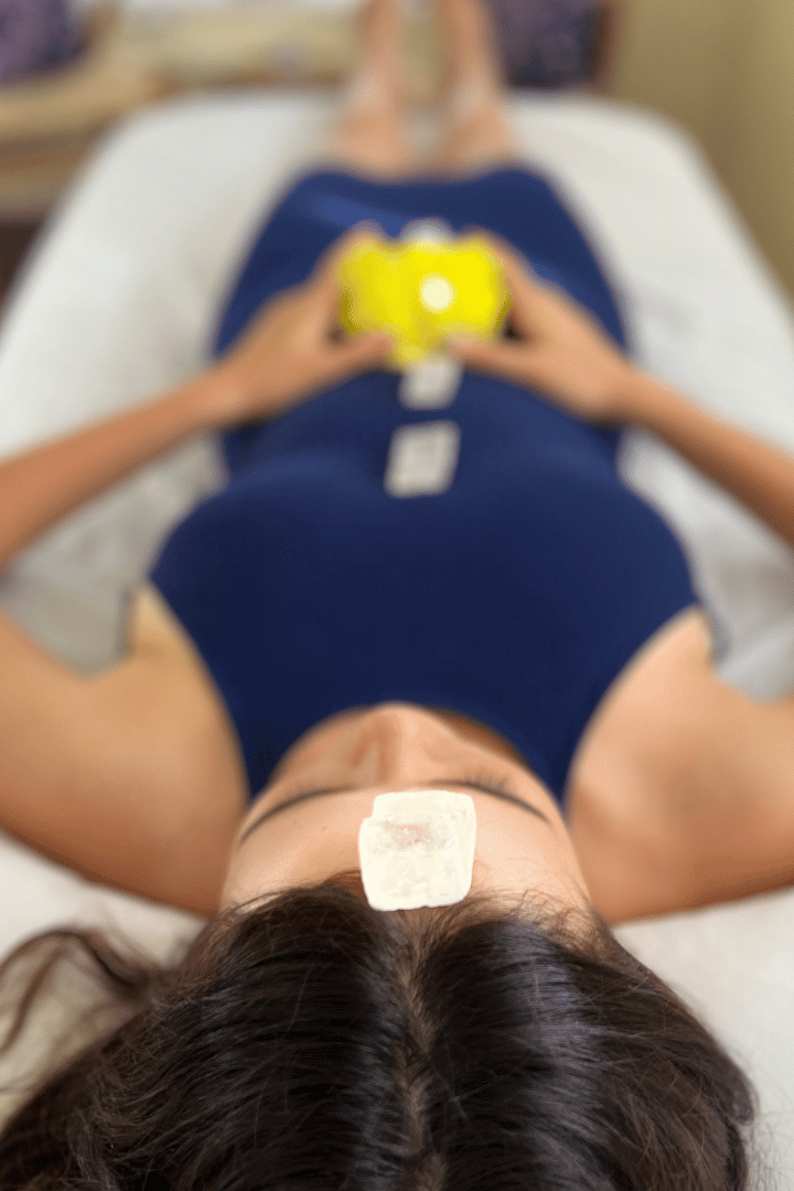 Person lying on a massage table receiving a crystal resonance session with Crystalogist, Brittain Cooper. Yellow sulfur and clear rhomboid calcite.