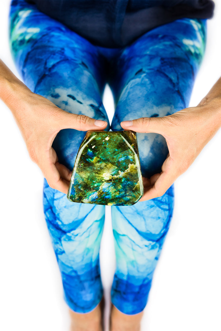Hands holding a polished labradorite specimen against blue and teal leggings printed from labradorite