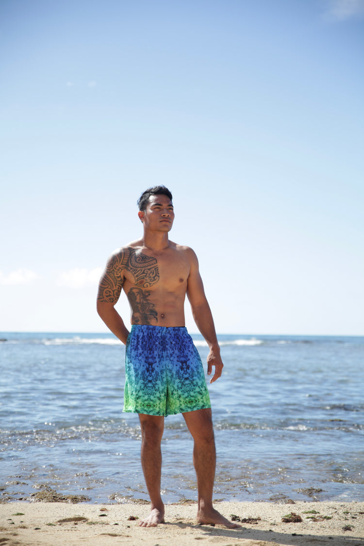 Man standing on the beach in blue and green crystal-print swim shorts