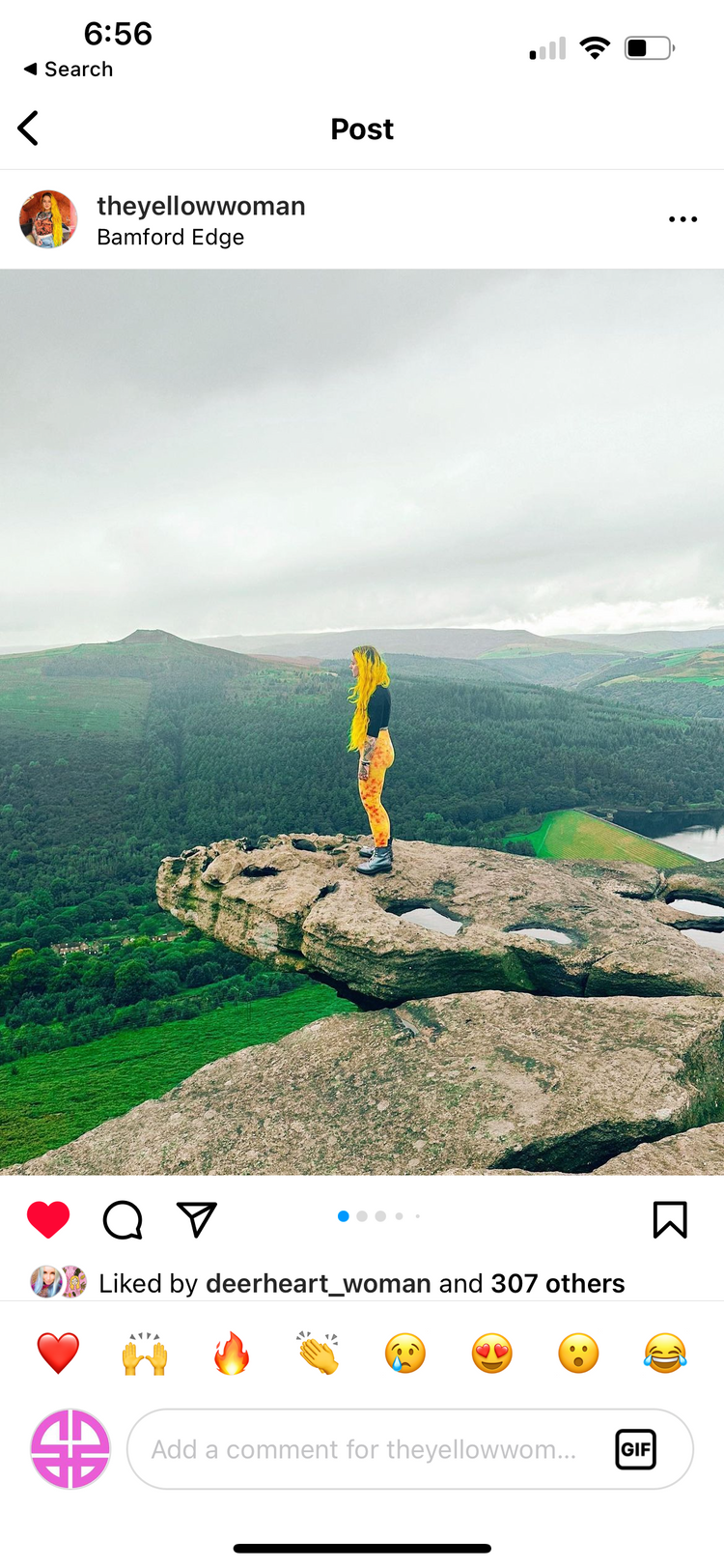 Woman in yellow printed leggings standing on a rock ledge above a green valley