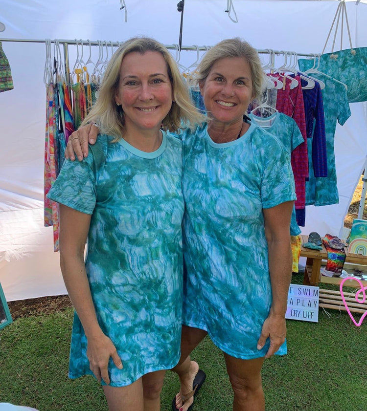 Two smiling women in matching teal and blue print tees at a market stall