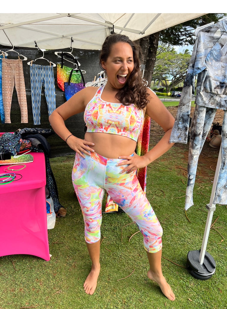 Woman laughing with hands on hips in a matching pastel tie-dye print sports bra and capri leggings at a market booth