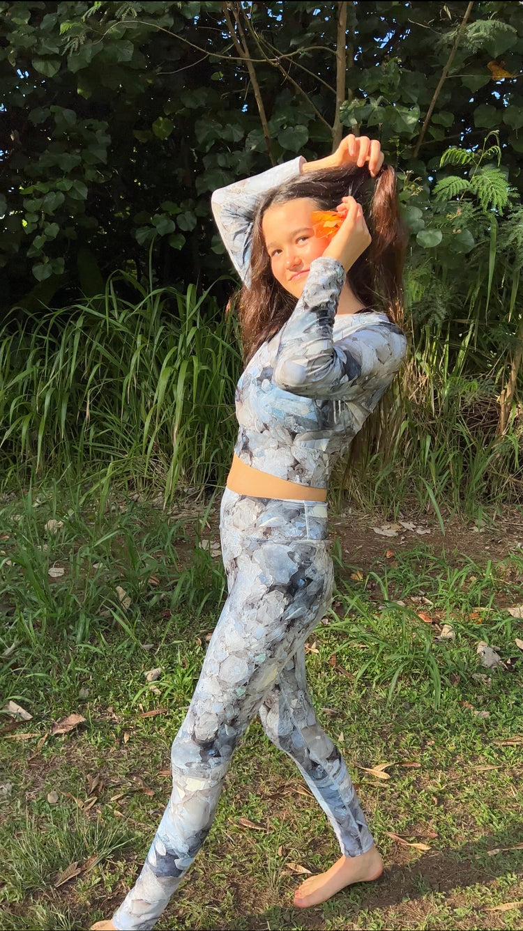 Girl posing on grass in a matching grey stone-print long-sleeve crop top and leggings