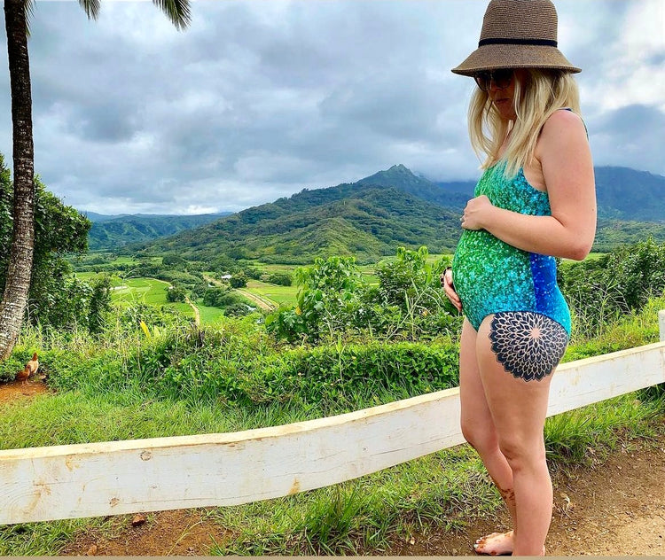 Pregnant woman in a green and blue printed swimsuit overlooking a lush green valley