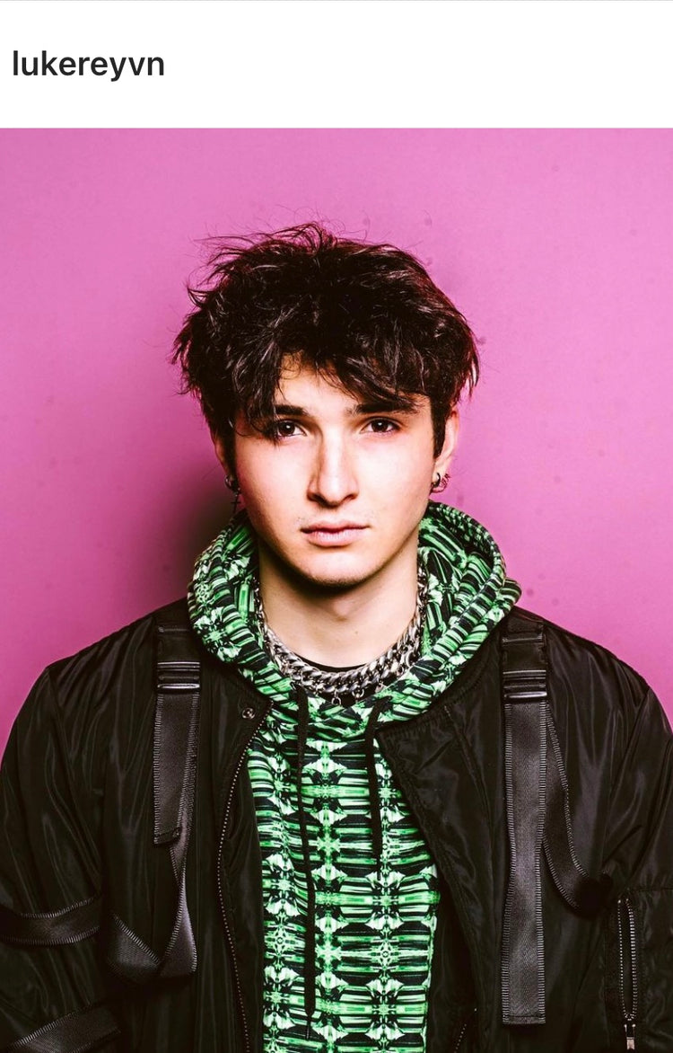 Young man in a green crystal-print hoodie and black jacket against a pink wall