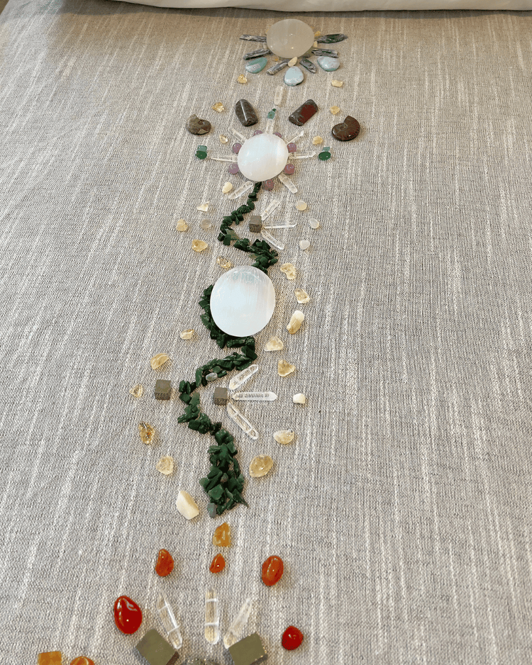 A crystal layout of polished spheres, clear quartz points and small tumbled stones arranged in a flowing line on natural linen